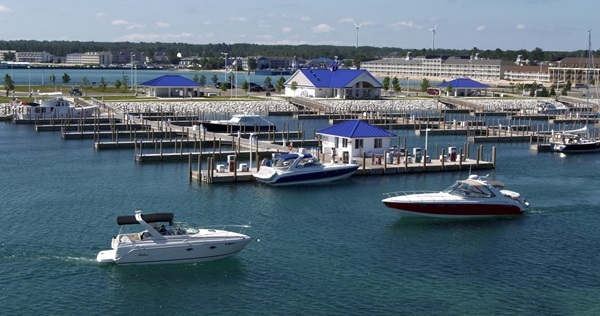 a few boats move through Mackinac Island State Harbor, with a few others moored at Mackinaw Marina on a clear, bright day