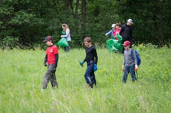 About a dozen adults and kids in long pants and long-sleeved shirts walk through a grassy state park area looking for invasive plants