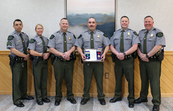 six officers stand in a hall smiling with an award