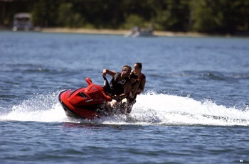 Two adults wearing life jackets ride a personal watercraft around a Michigan lake on a sunny day