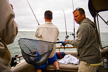 Anglers are shown fishing from a boat with a walleye in a landing net.