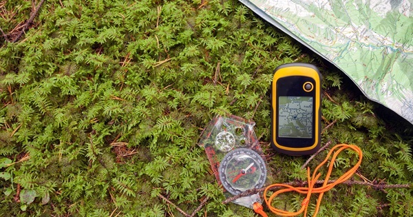 a compass with an orange lanyard, a yellow GPS unit and part of a paper, colored map lay on the grass