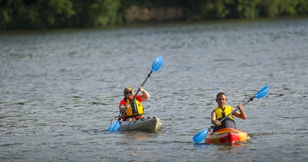 two people in yellow lifejackets solo kayaking on a lake on a bright day