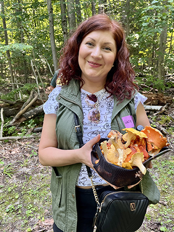 smiling student holds hat full of wild mushrooms