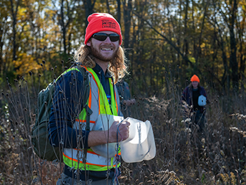 volunteer smiling at camera holding seed collector