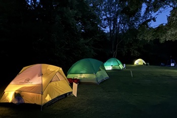 colorful yellow, green and blue pop-up tents are lit from the inside on a dark, clear night at Maybury State Park