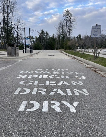 white painted letters spell "Stop Invasive Species. Clean, Drain, Dry" at the entrance to a state park boat ramp