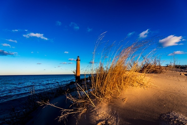 Little Sable Point Lighthouse stands against a crisp blue sky as the sun comes over the sand dunes along Lake Michigan