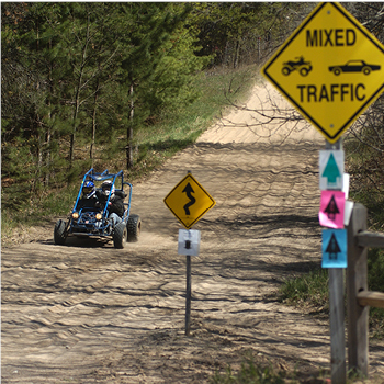 An ORV on a trail with signs in the foreground