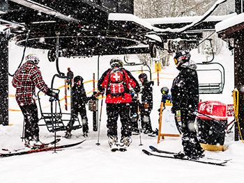 skiers and ski patrol waiting to get on triple lift with snow falling
