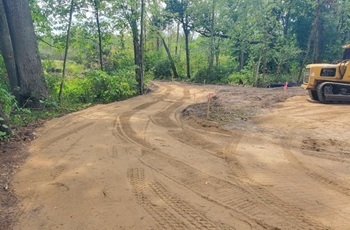 A graded, cleared area in a forested section of Gourdneck State Game Area, with heavy construction equipment just in view
