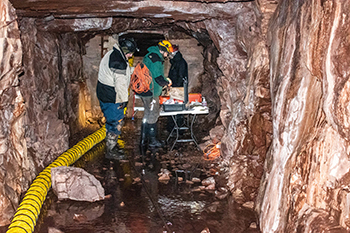 Workmen are show inside the Little Carp Mine installing an air hose to pipe in cold air.