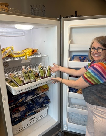 smiling woman in rainbow colored shirt gestures toward packages of ground venison in a freezer tray in an open freezer