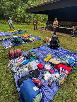 A tarp is shown spread out across the ground with campers' unnecessary items.