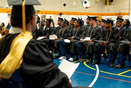 Graduates in their caps and gowns listening to a speaker in an assembly room