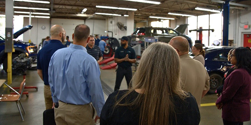 People gathered around a man speaking in an automotive garage
