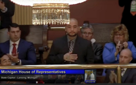 Man in a suit with hand over his chest during a Michigan House of Representatives gathering