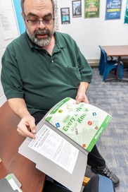 Man wearing glasses presenting a folder containing a magazine and some paper work.