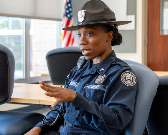 A woman with black hair sits and is speaking in a corrections uniform