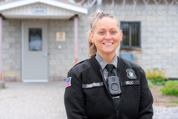 a blonde woman stands in front of a door in a corrections uniform