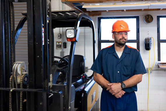 A male prisoner stands next to a forklift in a workshop