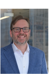Ben Stupka wearing a blue suit and glasses for his headshot