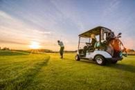 A man teeing off beside a golf cart on a golf course.