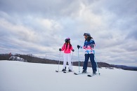 Two women on skis standing at the top of a snowy slope. 