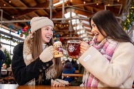 Two women in winter clothing toasting with glasses of beer. 