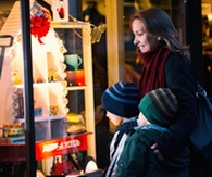 A woman and two children looking at a holiday display in a store window. 