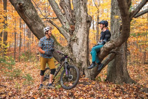 A man and woman with mountain bikes on a trail in a forest. 