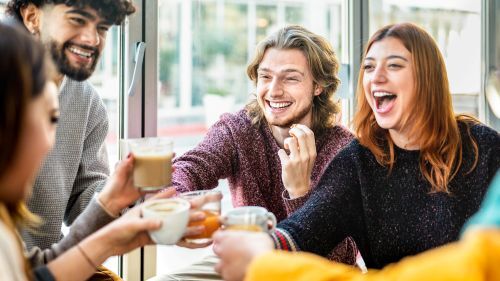 A group of friends toasting hot beverages around a table. 