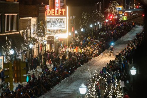 A crowd of spectators cheering as a dog-sled team races by in downtown Marquette. 