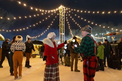 People gathered around a light display outside at night during winter. 