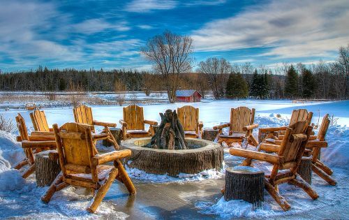 A circle of wooden chairs around a firepit during winter. 