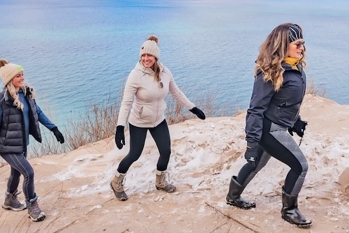 Three women in winter gear hiking along the Lake Michigan coast. 