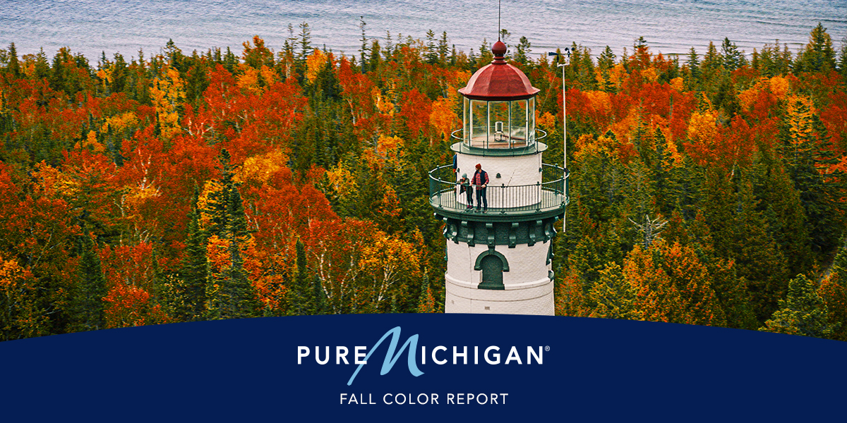 A family with two children on the observation deck of a lighthouse overlooking a fall forest and Lake Huron shore. 