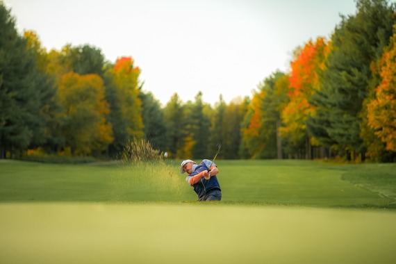 Man swinging golf club with fall trees behind him