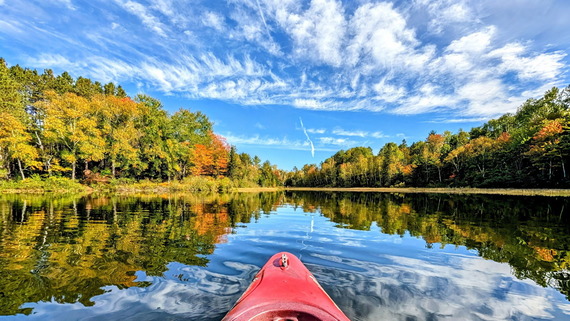 A red kayak floating in the middle of a lake with trees changing color in the background