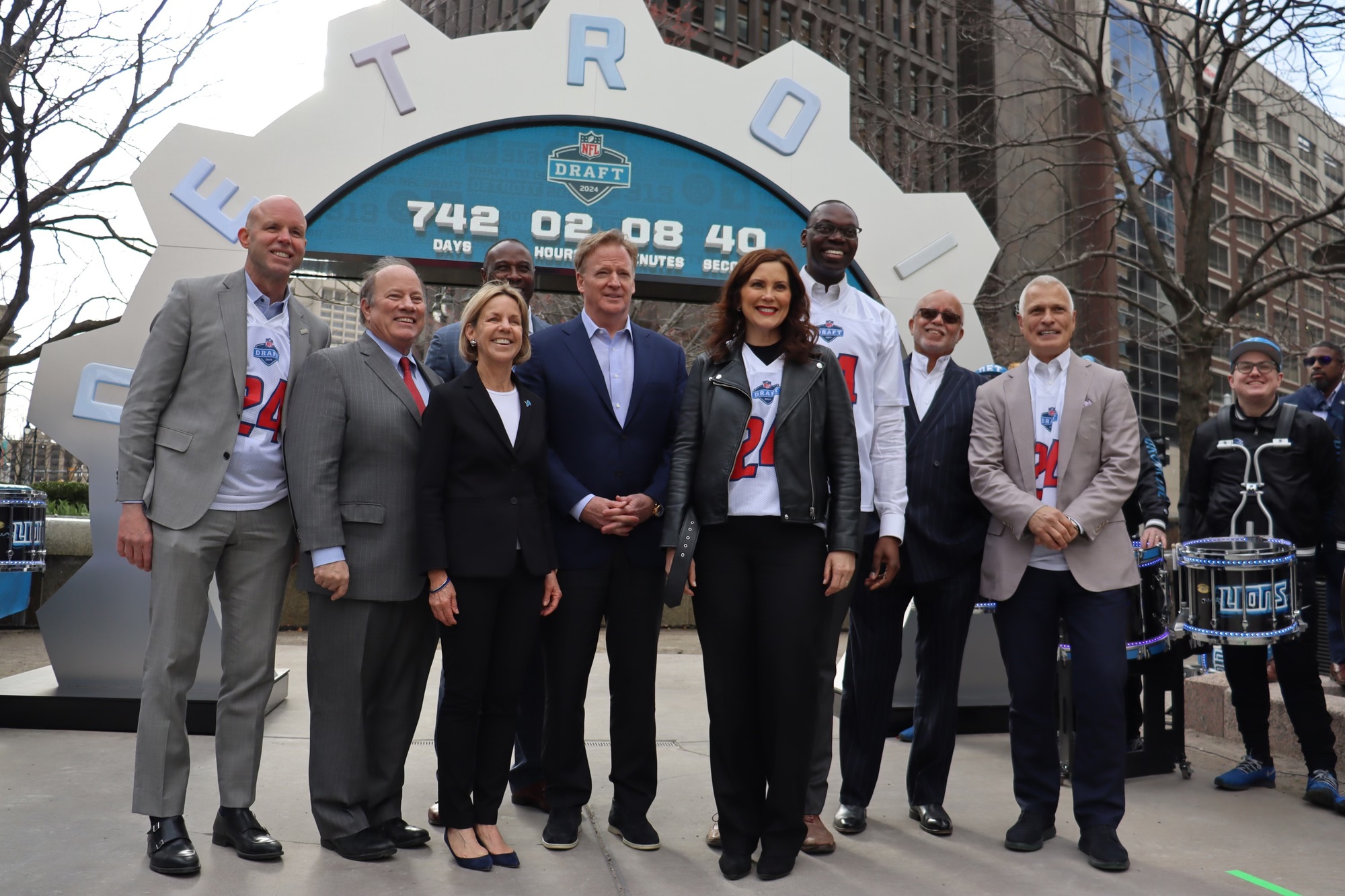 Group photo including Gov. Whitmer, Lt. Gov, Roger Goodell, and other people standing in front of countdown clock for the 2024 NFL Draft