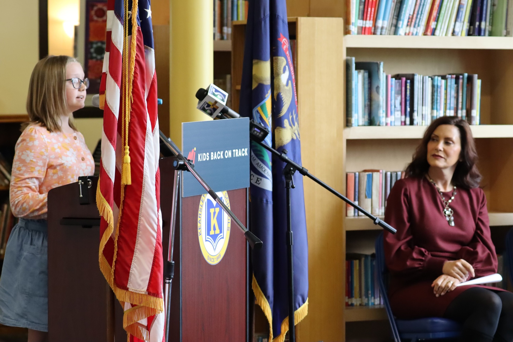 Governor Whitmer listens from a stage as a student named Caroline at an event announcing the Mi Kids Back on Track plan.