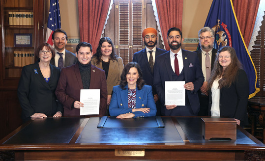 Rep. Puri and Rep. Noah Arbit, holding their signed laws, stand with Gov. Gretchen Whitmer and stakeholders.