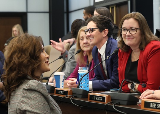 Rep. Price listens on a dais with fellow House representatives while Gov. Whitmer speaks to them.