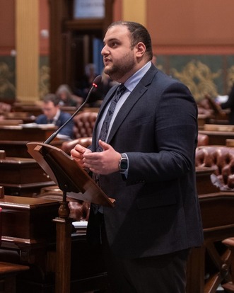 Rep. Alabas Farhat speaks at a podium on the floor of the Michigan House of Representatives.