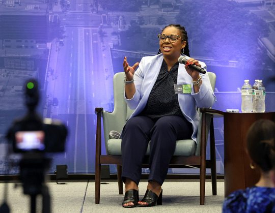 ALT.TEXT Seated on stage, speaking to a crowd, State Rep. Kristian Grant (D-Grand Rapids) speaks as part of the American Planning Association Housing Conference panel on Aug. 20, 2024.