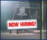 Photo of Store window with a NOW HIRING sign in it.