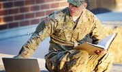 man in army fatigues looking at laptop 