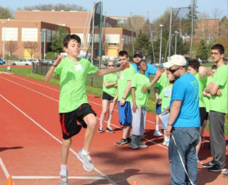 Boy running on track with other students and coach looking on