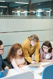 Instructor leaning explaining something on the table to the three students around her