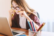 Woman sitting in front of open laptop with pencil between her teeth